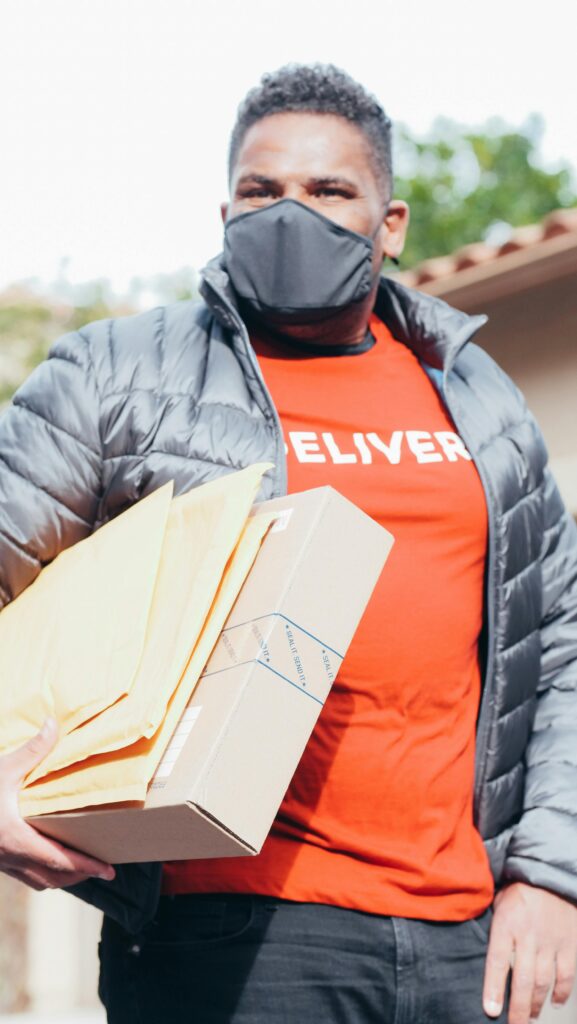 Delivery man in facemask holding packages, embracing new normal safety measures.